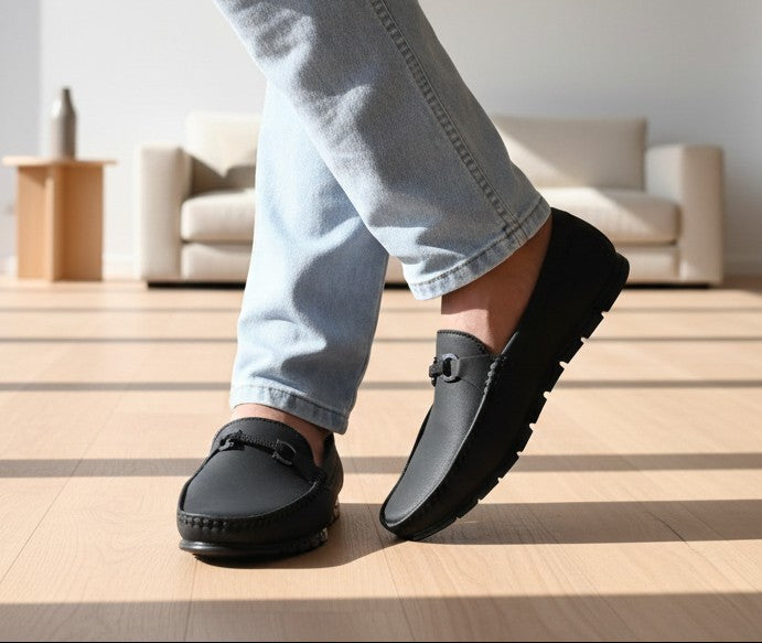 Person wearing black ZAWA Monarcha loafers on a wooden floor with a neutral background