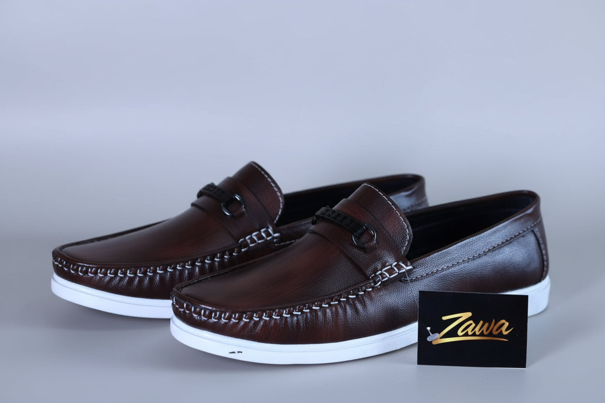 Pair of brown loafers with white soles on a wooden surface, featuring the Zawa brand logo.
