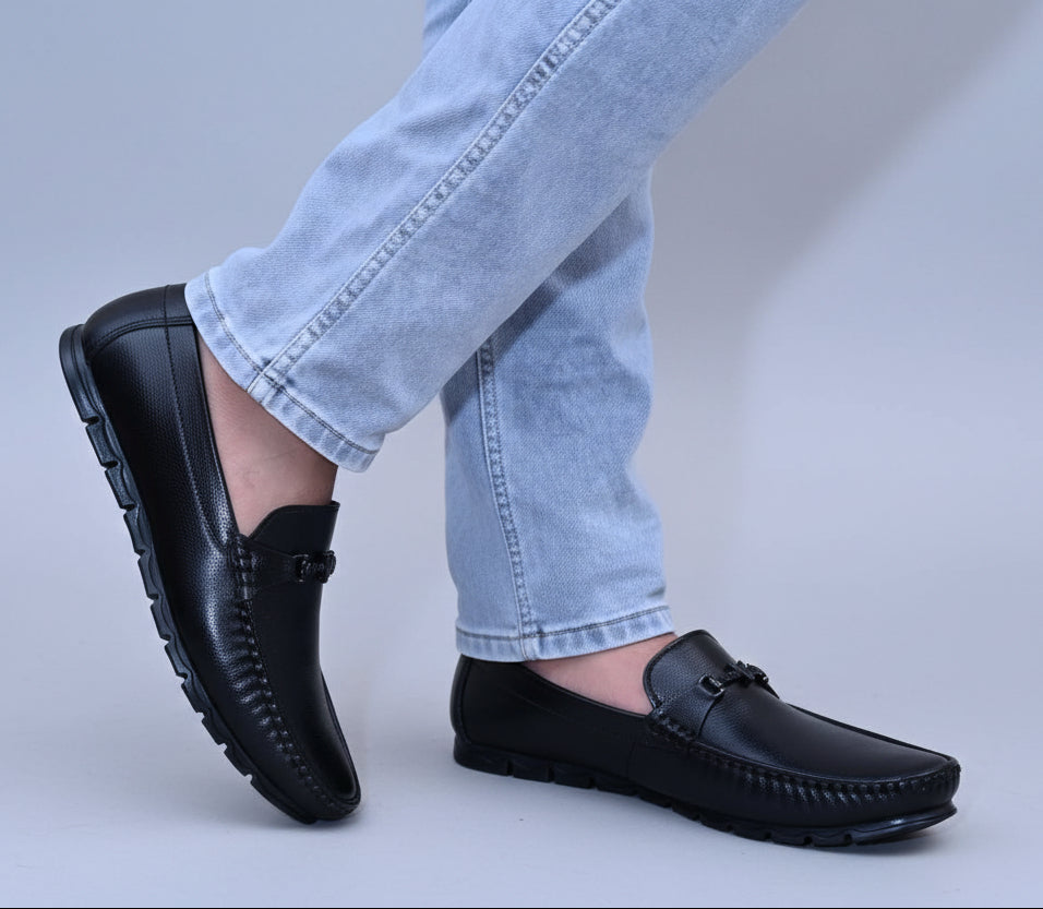 Black loafers worn with light blue jeans on a plain surface.