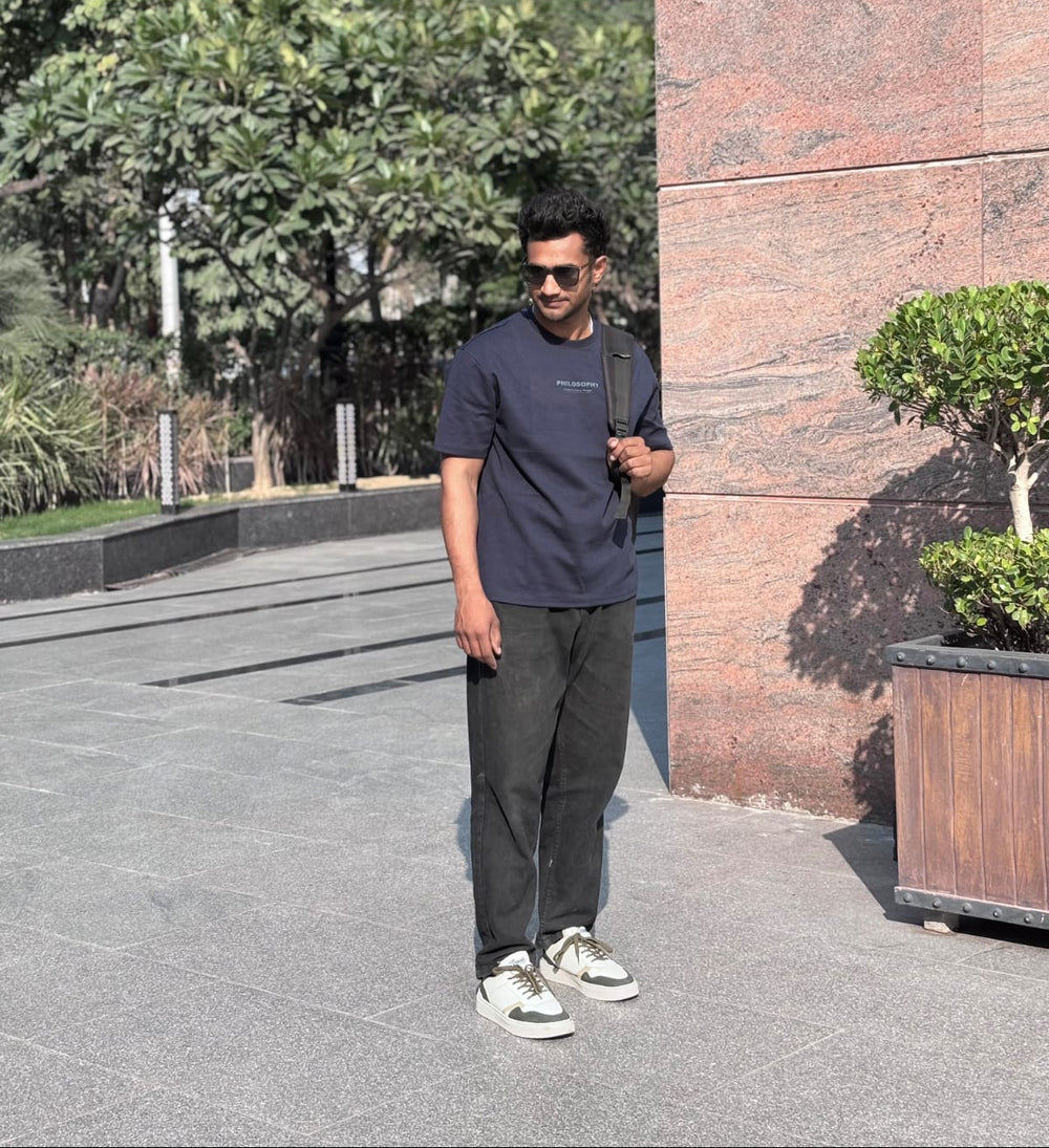Man standing outdoors near a brick wall with trees in the background wearing zawa sneakers