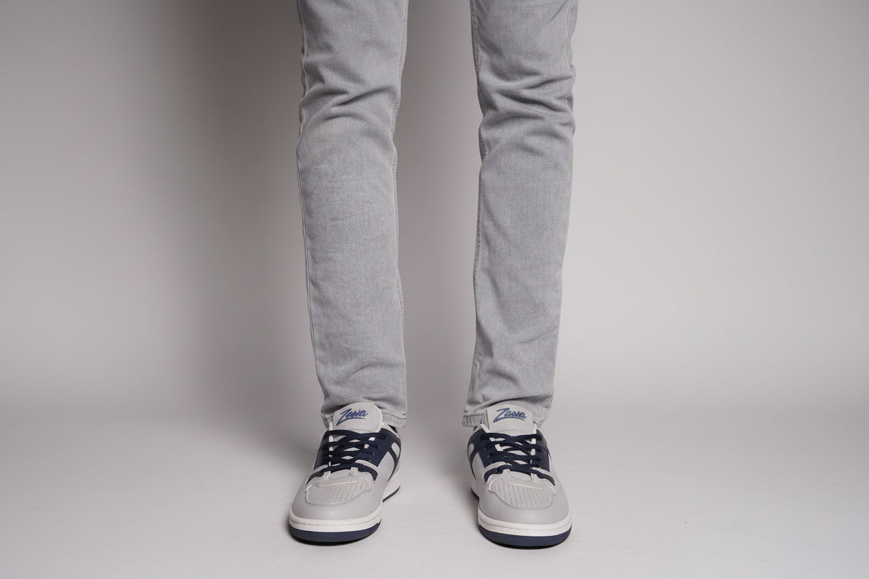 Gray pants and gray sneakers on a person standing against a grey background