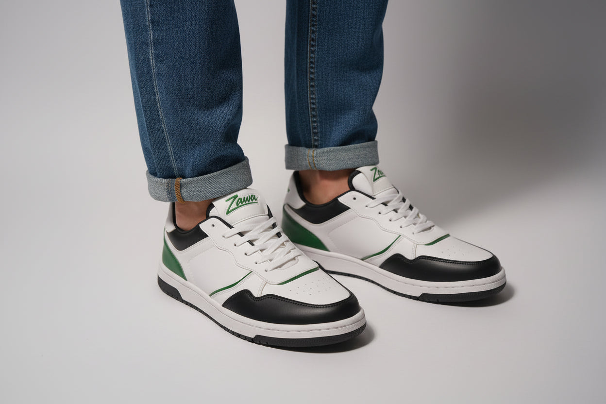 White and black zawa noctyra sneakers with green accents worn with a blue jeans on a gray background